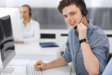 Call center. Group of casual dressed operators at work. Focus on young businessman in headset at customer service office. Telesales in business