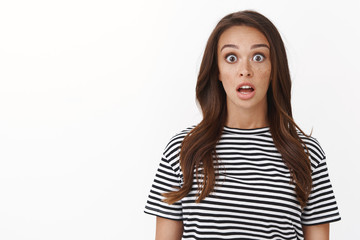 Surprised speechless cute brunette girl in striped t-shirt drop jaw from amazement, stare camera...