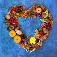 Heart shaped Autumn and fall wreath with a variety of natural flora, fauna and food on mottled blue background. Harvest festival theme.