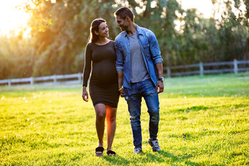 Beautiful pregnant couple relaxing with a walk in the park at sunset.