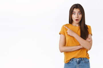 Surprised, amazed good-looking girl gossiping with friend, stare amazed, widen eyes folding lips, say wow as pointing upper left corner, heard rumor about coworker standing near, white background