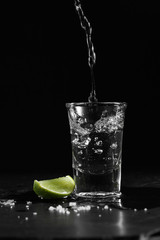 Pouring vodka into the shot glass on a black background with a blank space for a text, Russian vodka with salt and lemon