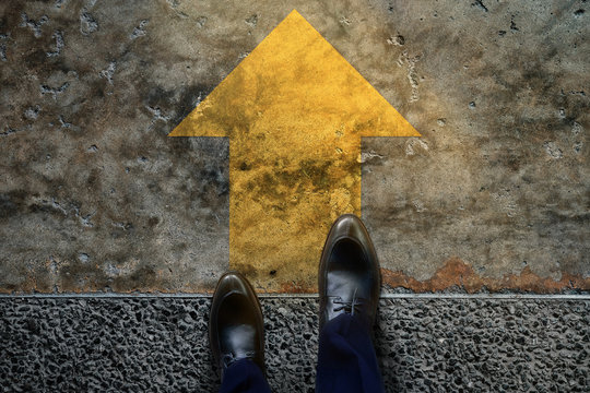 Start And Challenge Concept. A Business Man On Formal Shoes Steps To Follow A Yellow Arrow, Get Ready To Moving Forward Or Take A Chance To Success. Top View