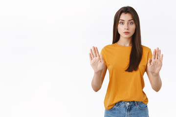 Serious-looking confident good-looking woman in yellow t-shirt, raising hands in stop, taboo or...