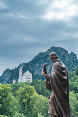 Castle of Louis II of Bavaria, the most visited monument in Germany, in the afternoon with blue and brown tones and the green meadow in the background with the sky covered with gray clouds.
