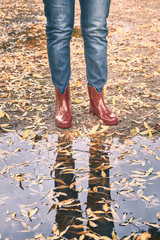 red rubber boots in front of a puddle with yellow leaves in autumn
