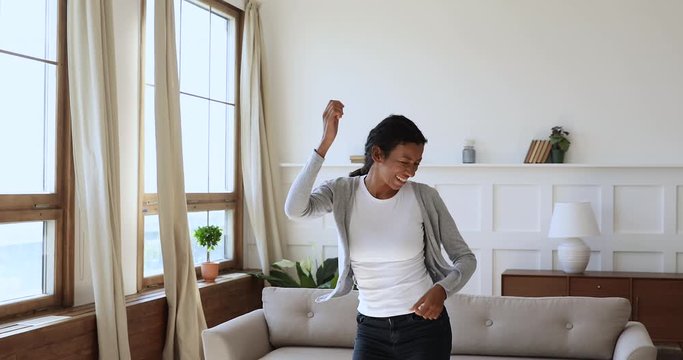 Carefree overjoyed african woman jumping dancing alone at home