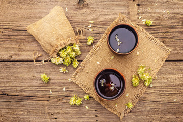 Cup of calming herbal tea with fresh wild hops. Hops cones in sack on vintage boards background