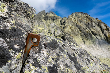 Angle piton embedded in the rock in the background a mountain ridge. A piton made of steel sheet bent into V shape. Work well for larger cracks. - 296918646