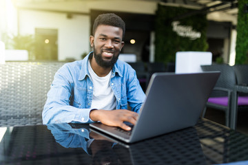 Portrait of a smiling african man with laptop at cafe