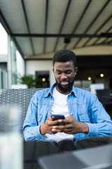 Young Afro American man sitting in cafe and use cell phone.