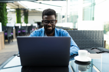 Handsome african businessman having online meeting on laptop in a cafe and drinking coffee