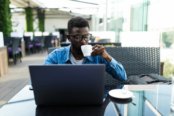 African man sitting at table in cafe working with laptop and papers and drinking coffee