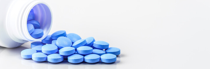 Blue pills are scattered from a jar on a white background.