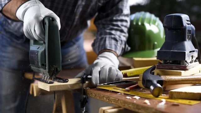 Adult carpenter craftsman wears protective leather gloves, with electric saw working on cutting a wooden table. Construction industry, housework do it yourself. Footage.