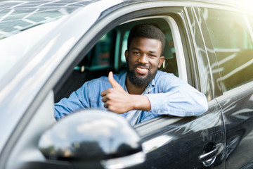 Young handsome african man show thumbs up while drive his car