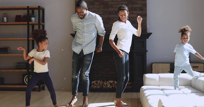 Joyful active african american family dancing jumping in living room