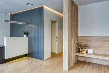 Modern design reception with desk, flowers, white walls and gray cellings. Wooden floor and screen. Corridor with white doors Dental clinic