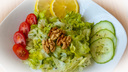 Frischer Eisbergsalat mit Tomaten Gurkenscheiben Zitrone Kräuterdressing Walnüssen bestreut mit frischen Kräutern angerichtet auf einem Weißen Teller