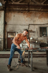 Muscled half naked man at work in an old factory.