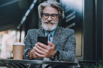 Smiling man in glasses is using smartphone