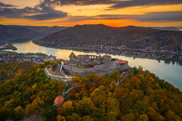 Visegrad, Hungary - Aerial drone view of the beautiful high castle of Visegrad with autumn foliage and trees. Dunakanyar and golden sunset at background