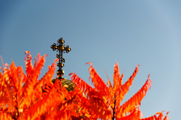 Orthodox cross on the church dome against the background of autumn orange leaves and clear blue sky. Outdoors. Daytime