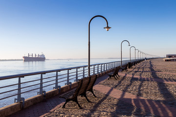 ROSARIO, ARGENTINA - JULY 6, 2019:  Riverside park next to the Parana River. Classic promenade in the Spain Park. Cargo ship at the background, anchored in the river.