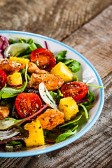 Salad with chicken, mango and tomatoes on wooden table