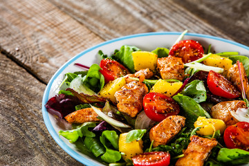 Salad with chicken, mango and tomatoes on wooden table