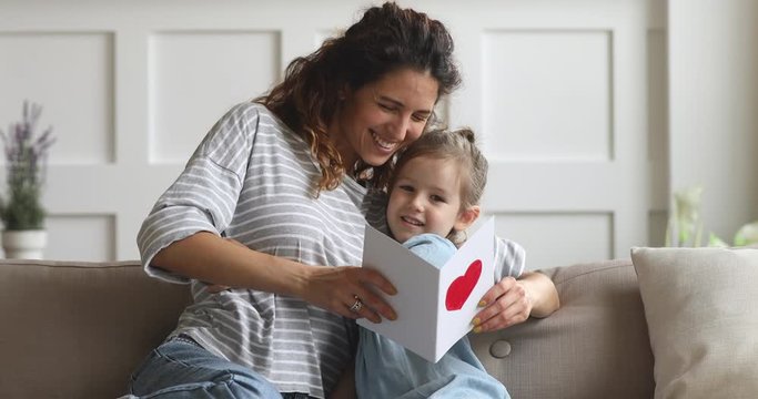Happy mom and little kid daughter holding reading greeting card