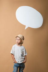 A boy in a hat stands on an orange background and shows different emotions. The boy is very happy. Of the boy there is an empty white speech