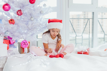 Pretty little girl is playing with decor snowflakes near New Year tree, smiling lovely.