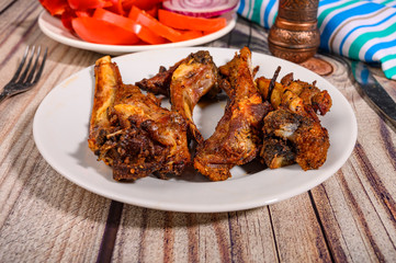 Lamb ribs marinated with spices grilled in a plate on the table. With sliced tomatoes, sweet peppers and onions.
