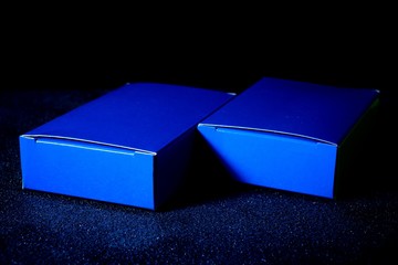 Two blue rectangular boxes lie on a black surface