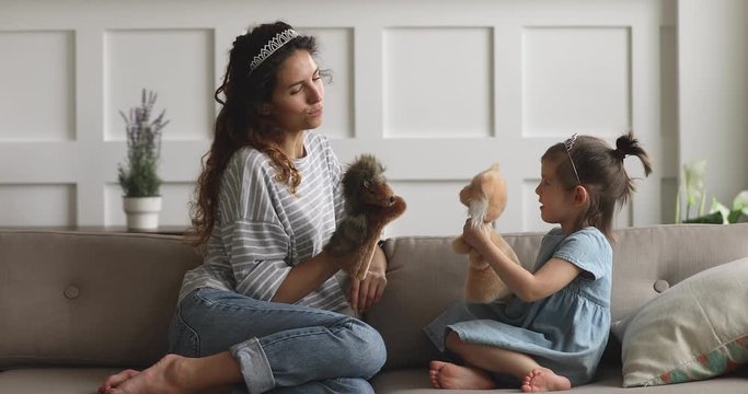 Happy mom wearing crown holding toys playing puppets with daughter