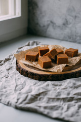 Fresh caramel fudge candies on a wooden plate with copy space in marble background