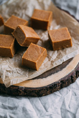 Fresh caramel fudge candies on a wooden plate with copy space in marble background