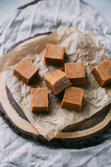 Fresh caramel fudge candies on a wooden plate with copy space in marble background