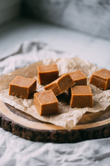Fresh caramel fudge candies on a wooden plate with copy space in marble background