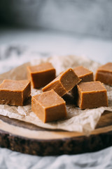 Fresh caramel fudge candies on a wooden plate with copy space in marble background