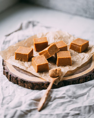 Fresh caramel fudge candies on a wooden plate with copy space in marble background