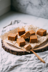 Fresh caramel fudge candies on a wooden plate with copy space in marble background