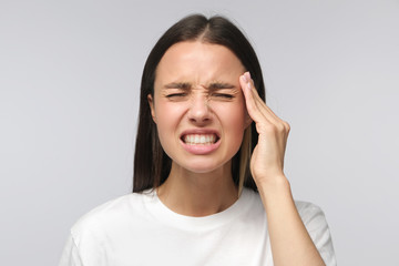 Portrait of young woman suffering from severe headache, pressing fingers to temples, closing eyes...