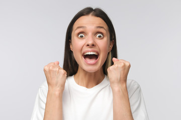 Young attractive woman shouting while her team win, raised both fist in victory gesture, isolated on gray background