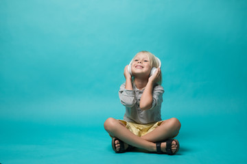 Very emotional boy listening to music on headphones on a blue background. The boy shows different...