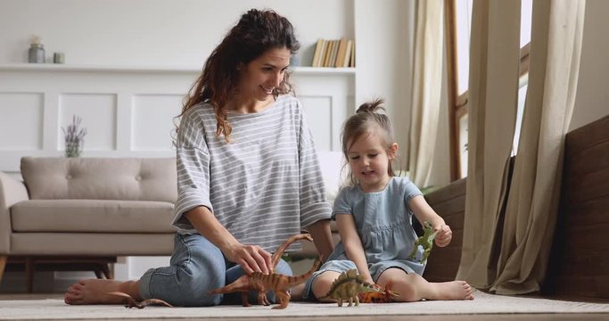 Happy mom with kid daughter playing dinosaurs sit on floor