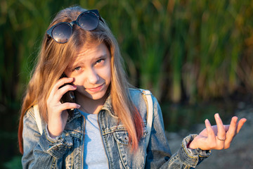 Young girl in an autumn denim jacket talking to her girlfriend on the phone and waving her hands emotionally