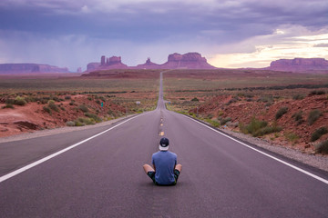 one young man sitting on the highway to monument valley at beautiful purple sunset