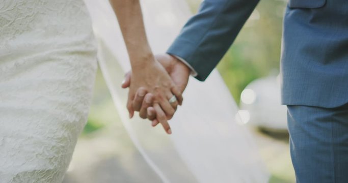 Close up shot of a bride and grooms hands interlocked showing a diamond ring, close up of couple holding hands on their wedding day walking together down the aisle